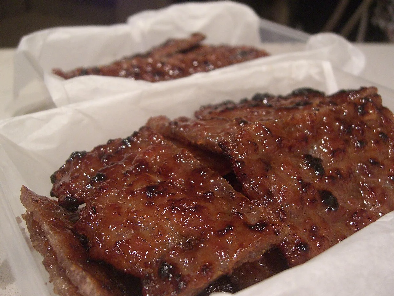 Glazed sheets of bak kwa rest in white paper.