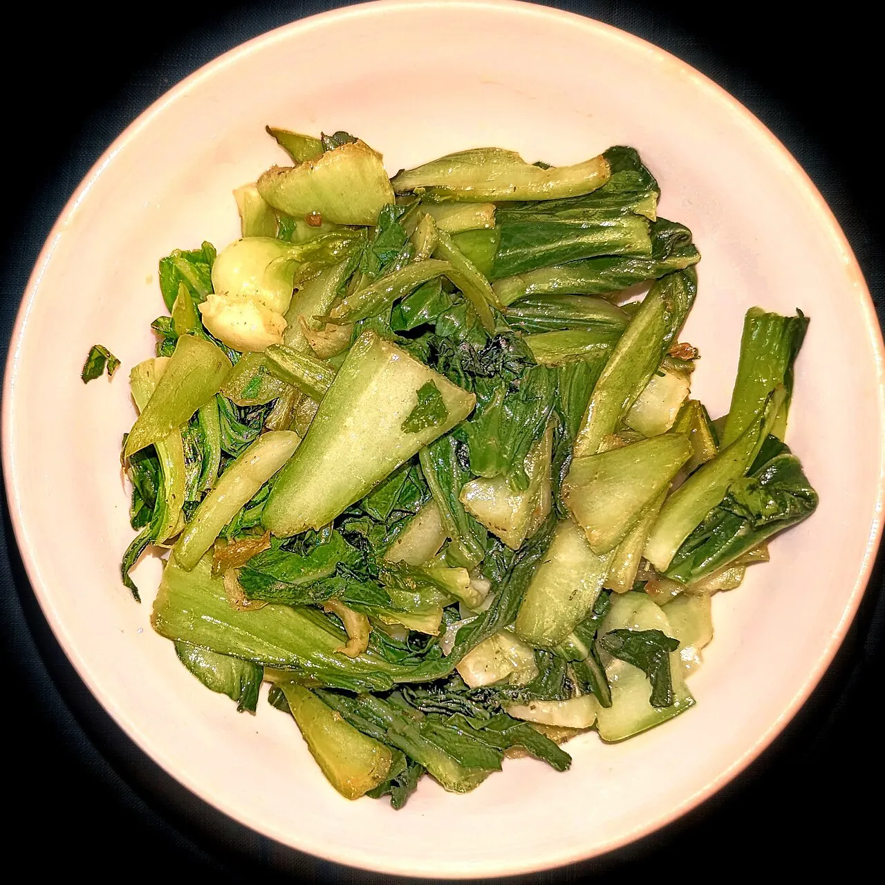 A pink plate contains sauteed bok choy pieces with green leaves and pale stems.