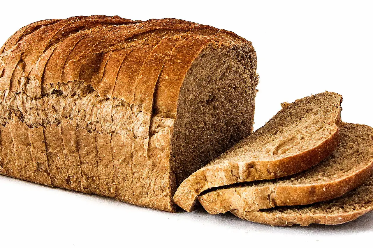 A loaf of brown bread sits on a white surface with three slices beside it.