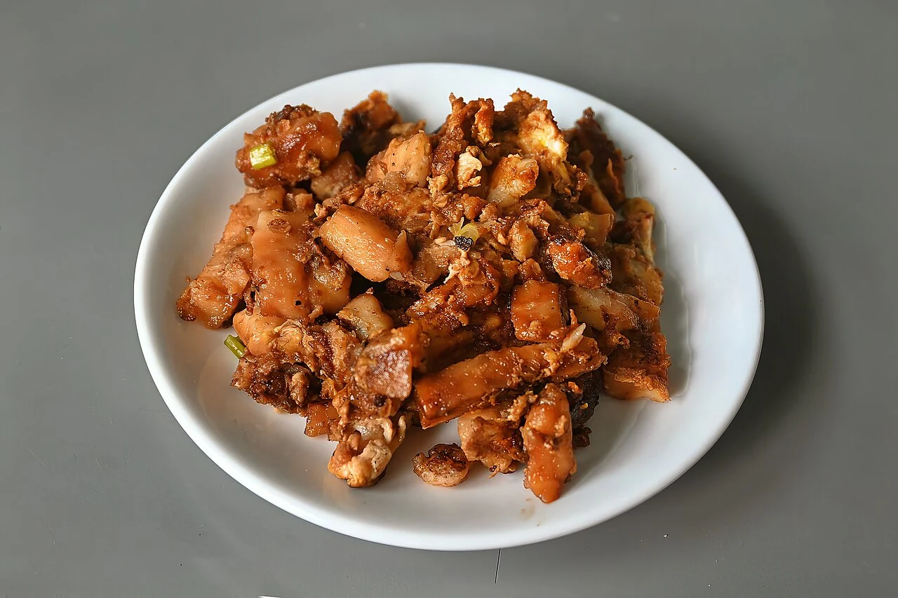 Fried cubes of carrot cake with egg and spring onion are piled on a plain white round plate.