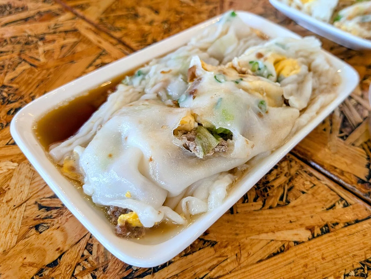 A plate of steamed rice noodle rolls with soy sauce and fillings.