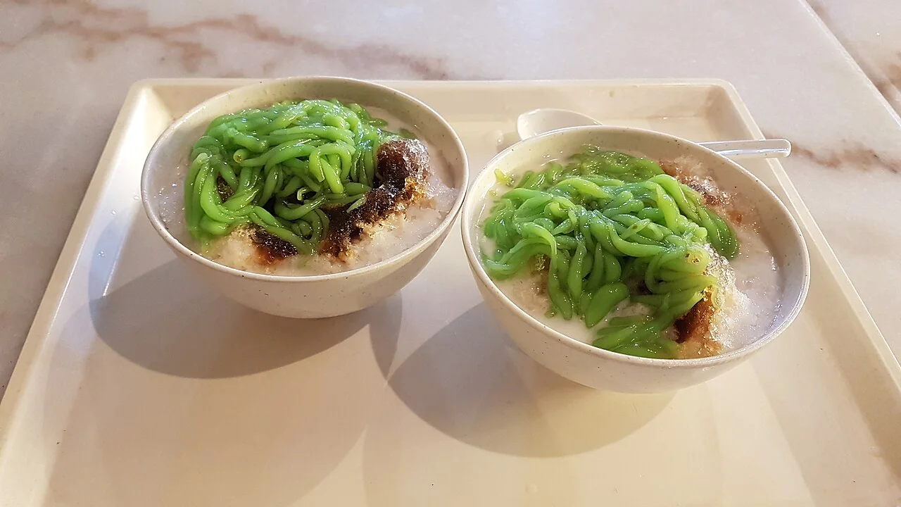 Two bowls of chendol with green jelly and coconut milk.