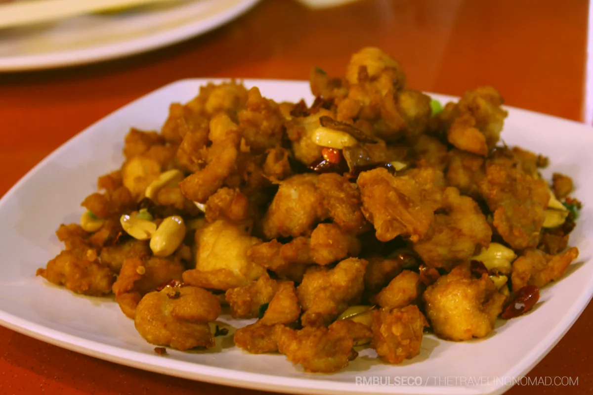 Fried chicken pieces with chillies and peanuts fill a white plate.