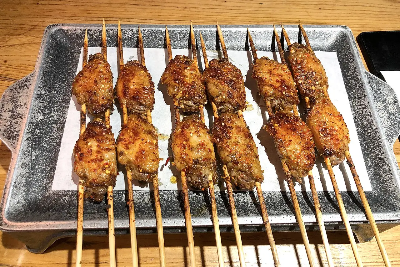 Grilled chicken wings on wooden skewers are arranged in two rows on a metal tray.
