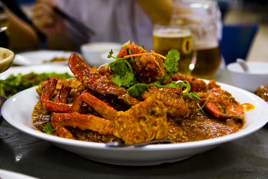 Bright red crab claws in thick orange sauce are topped with fresh coriander on a large white plate.