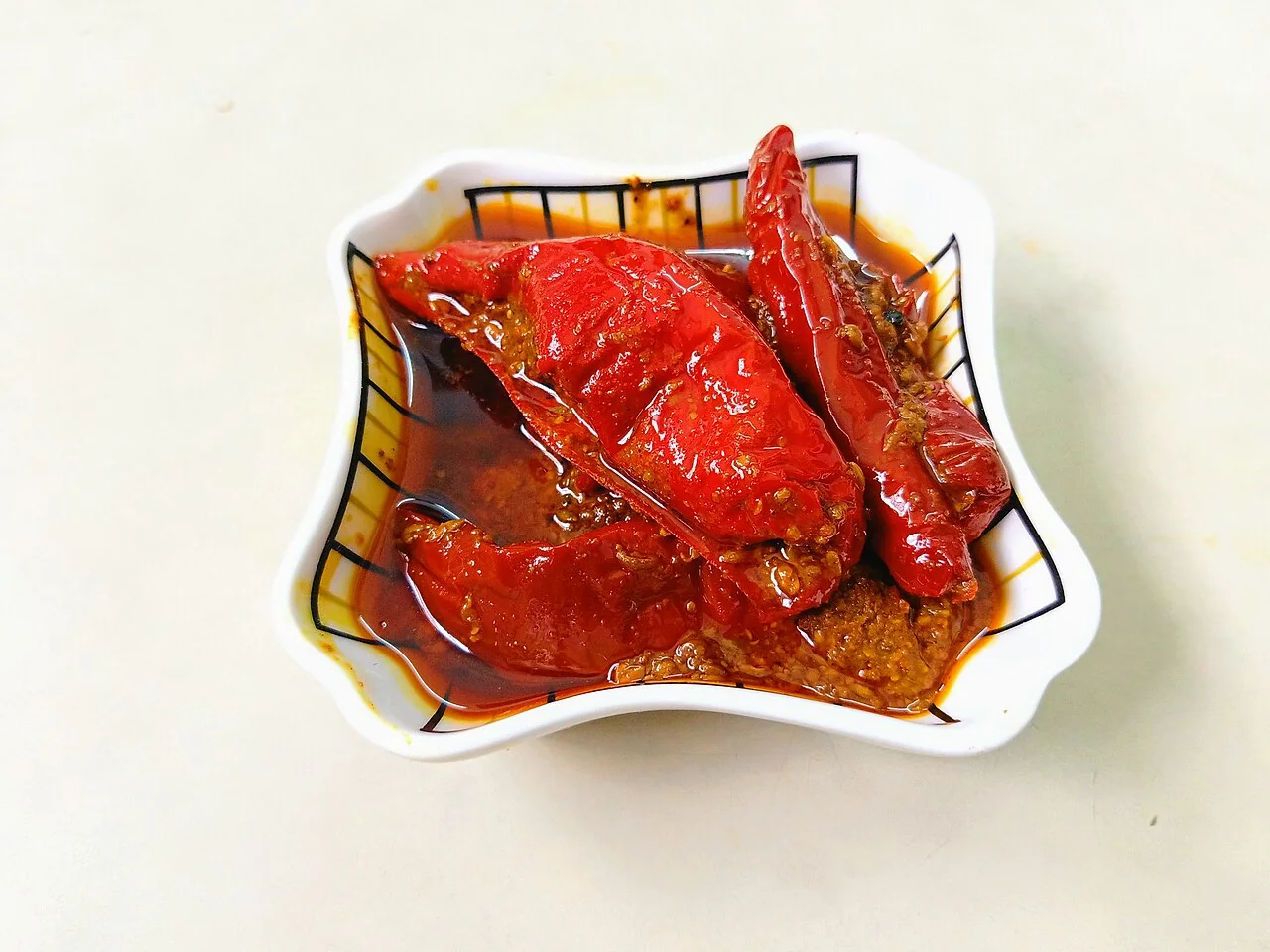 Red chillies preserved in oil and spices in a small white dish.
