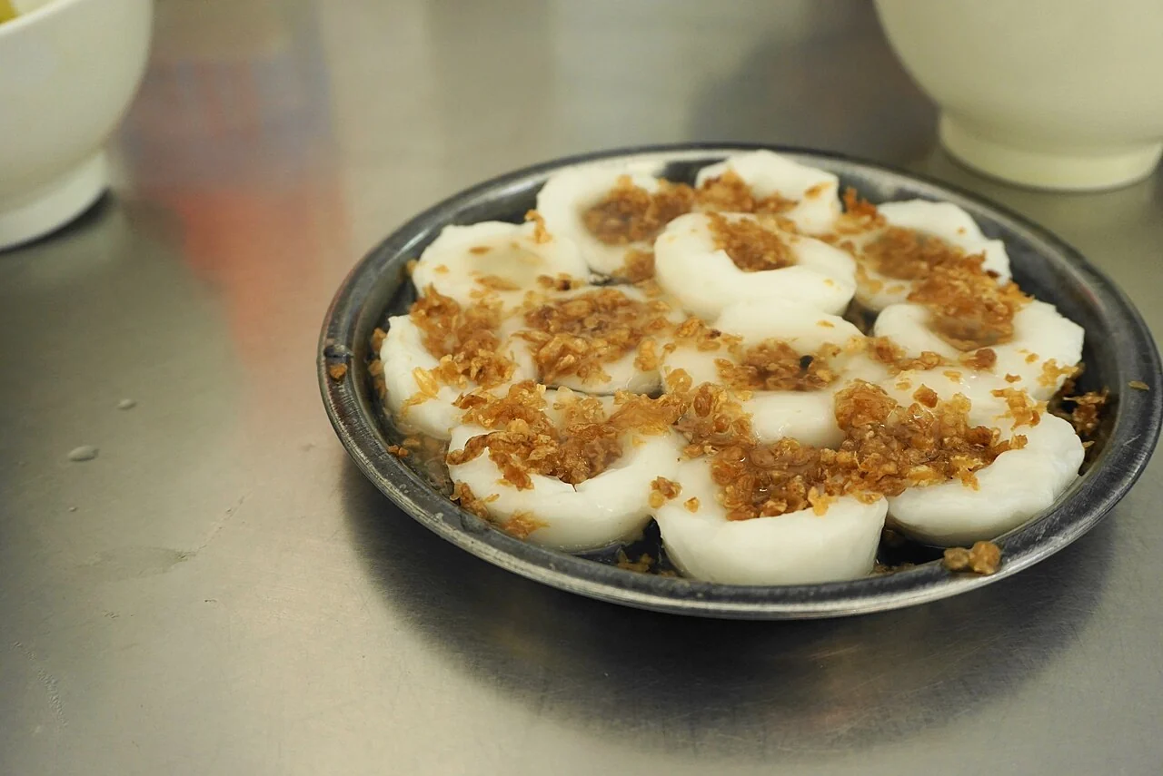 Several white steamed rice cakes sit on a round metal plate, each sprinkled with crispy golden-brown bits.