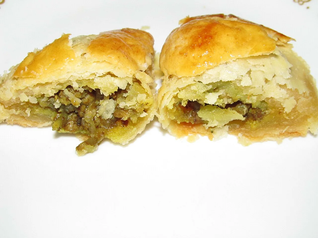 A curry puff is cut in half, revealing its greenish filling inside flaky pastry.