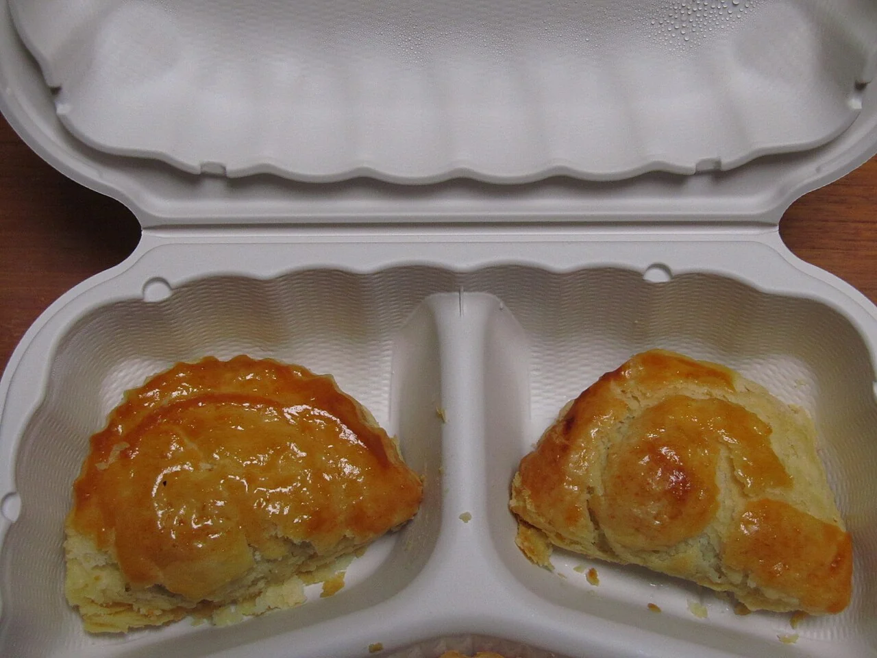 Two glossy, golden-brown baked pastries sit in the two compartments of an open white foam takeout container.