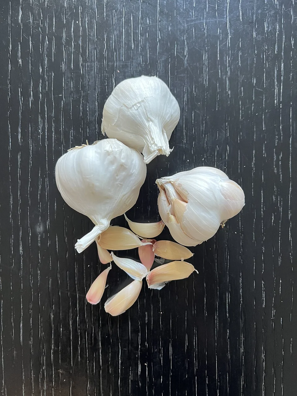 Three whole garlic bulbs and several cloves arranged on a dark wooden surface.