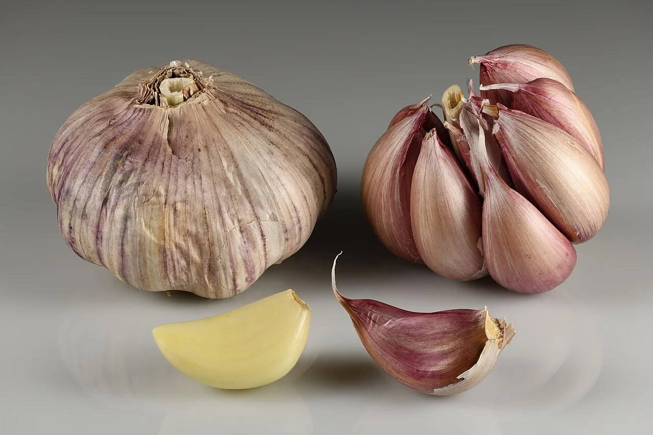 Whole garlic bulbs and individual cloves, including a peeled clove, on a neutral background.