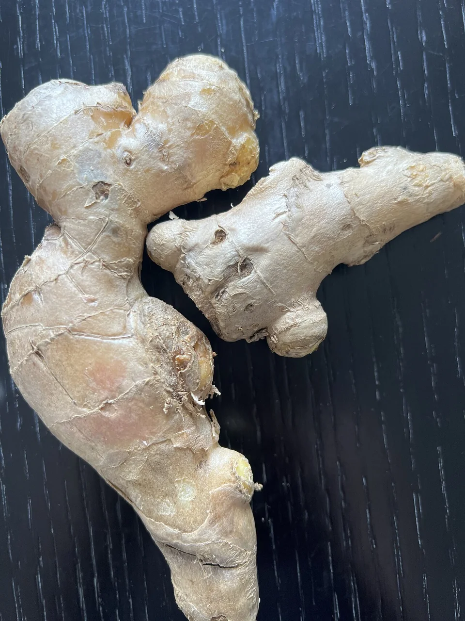 A branching piece of ginger with pale brown skin rests on a dark wooden surface.