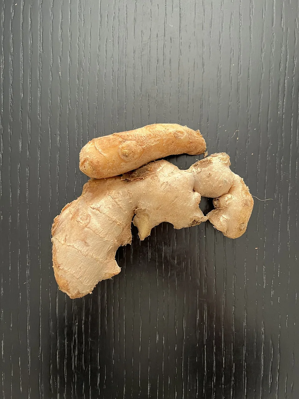 Knobbly pieces of ginger lie on a dark wooden surface.