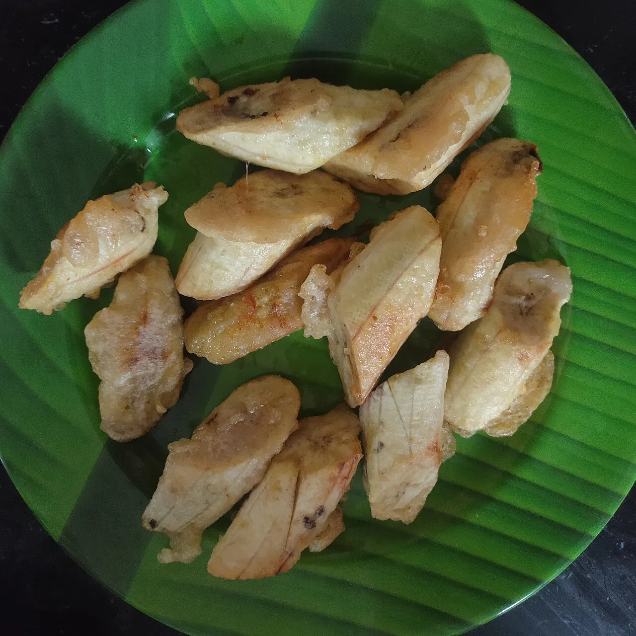 Slices of fried plantain banana fritters are arranged on a green plate.