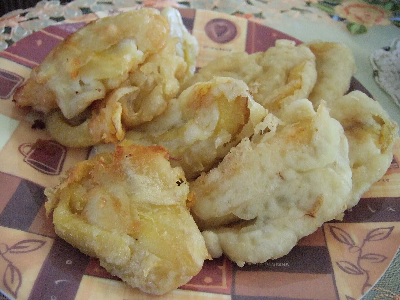 Several golden fried banana fritters are piled on a patterned plate.