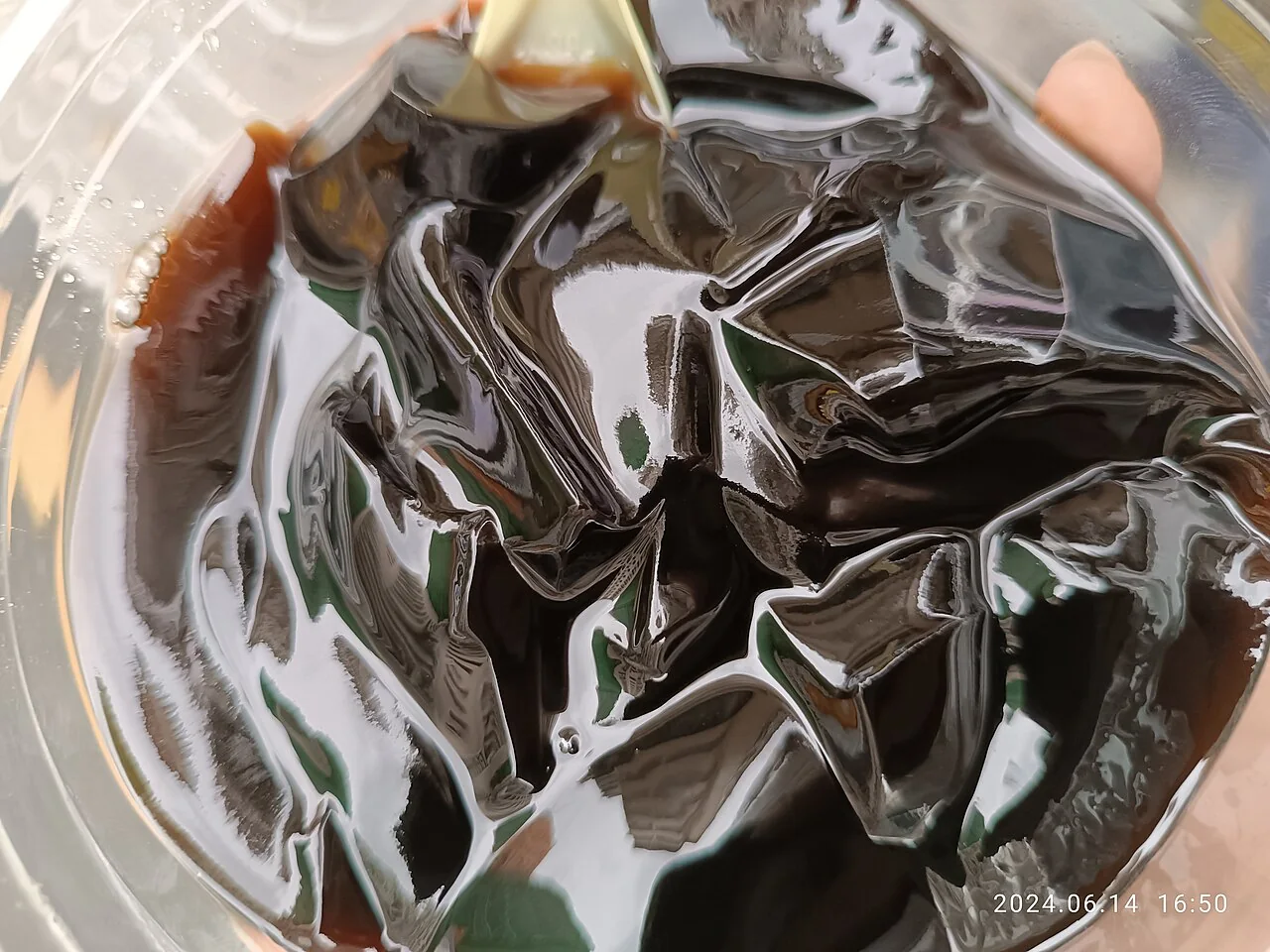 Glossy black cubes of grass jelly sit in a clear plastic container with dark syrup.