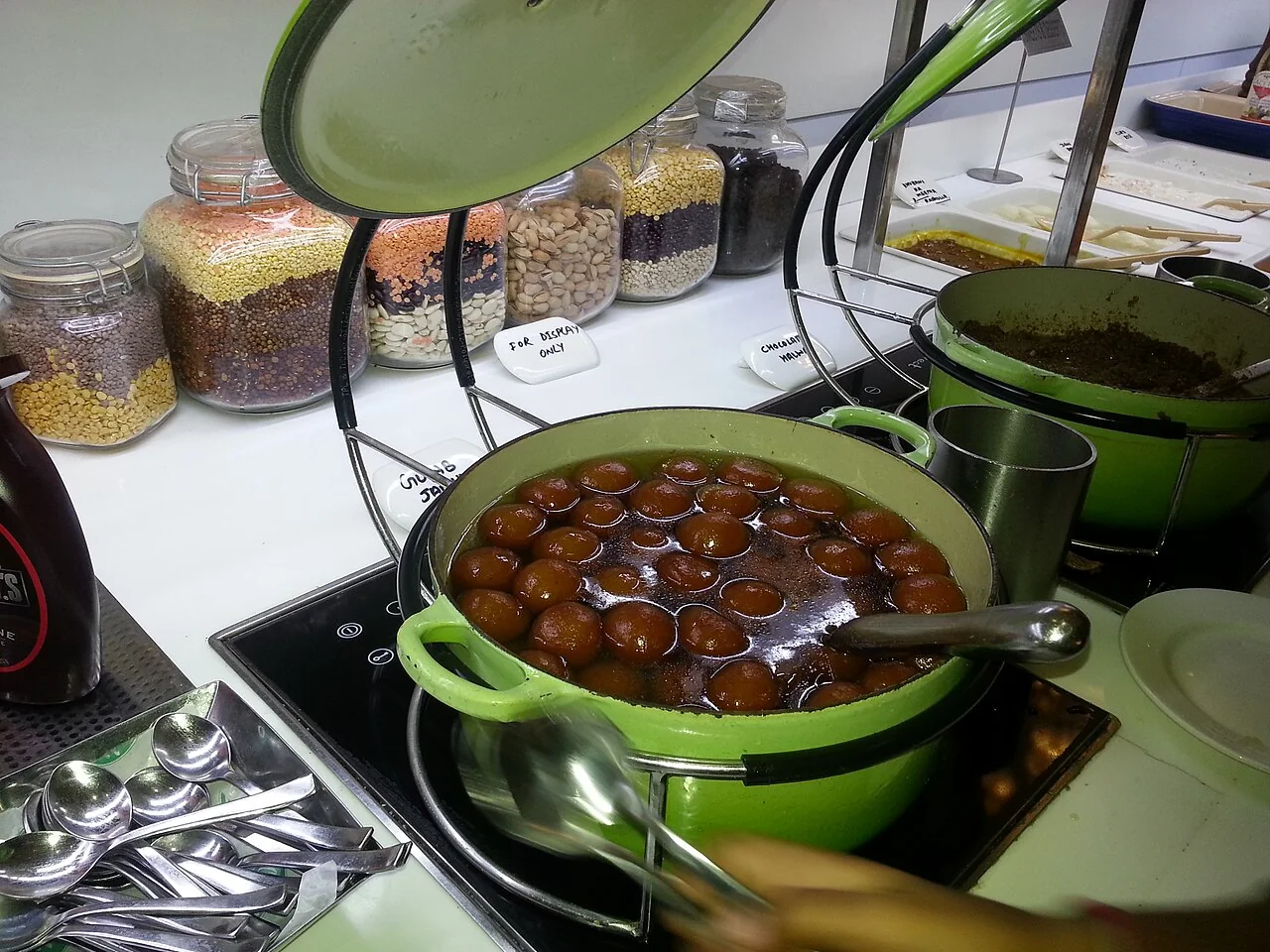 A green pot filled with gulab jamun soaking in syrup on a buffet counter.