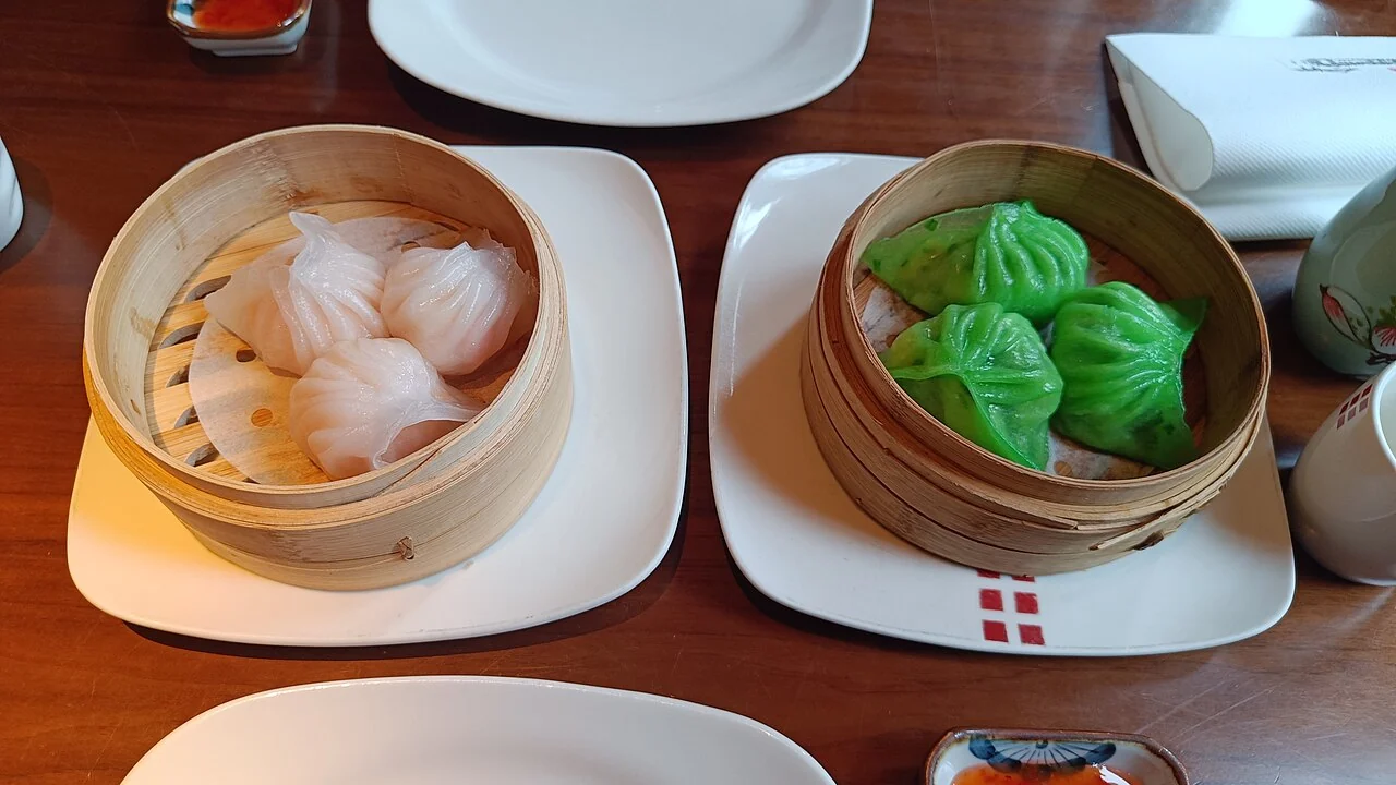 Two bamboo steamers hold dumplings: pale ones on the left and bright green ones on the right.