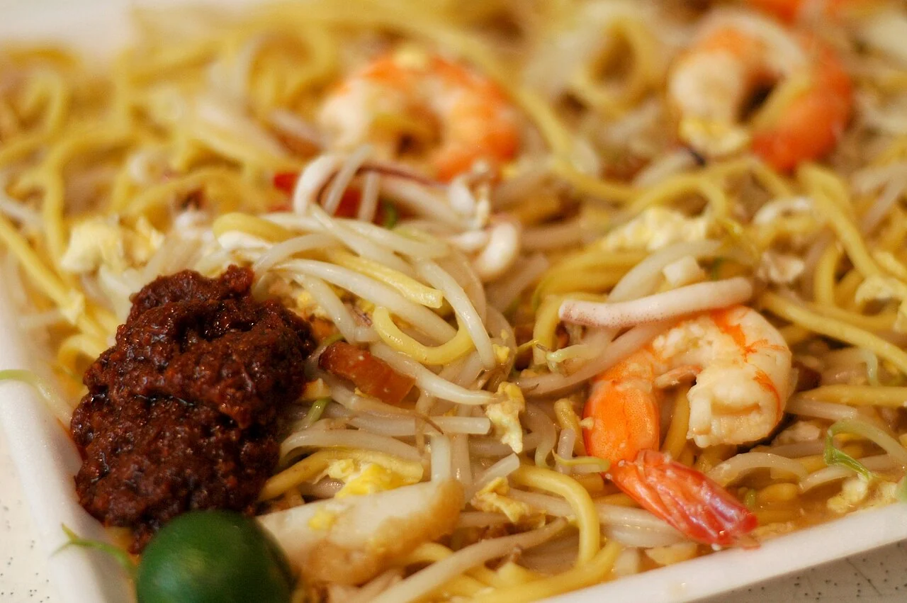 Close-up of fried noodles with prawns, squid, bean sprouts, egg and a spoonful of chilli paste.