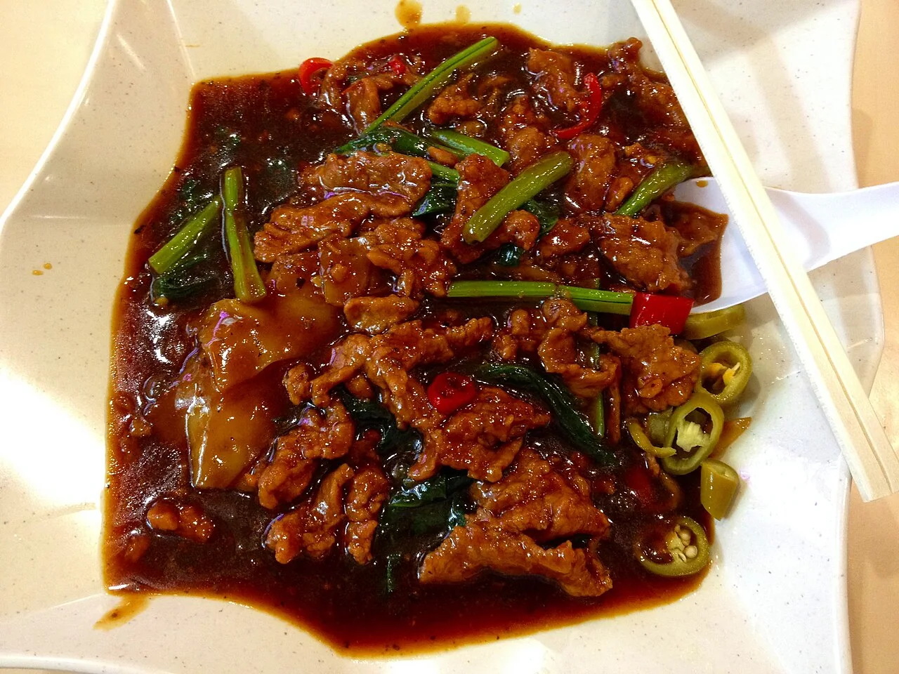 A plate of beef hor fun with thick gravy, sliced beef and green vegetables.