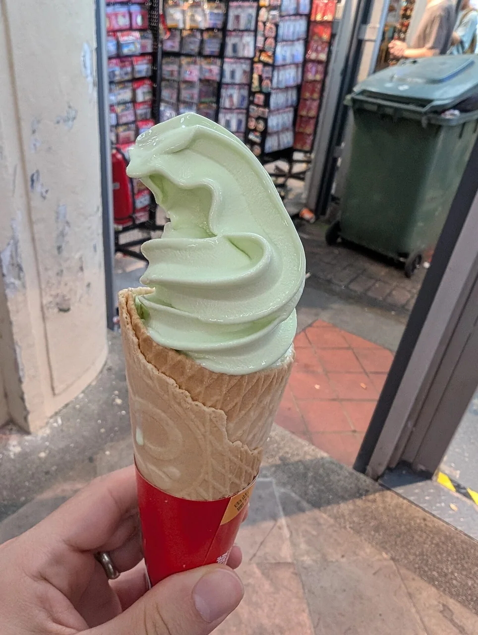 A hand holds a green honeydew melon soft-serve ice cream cone.