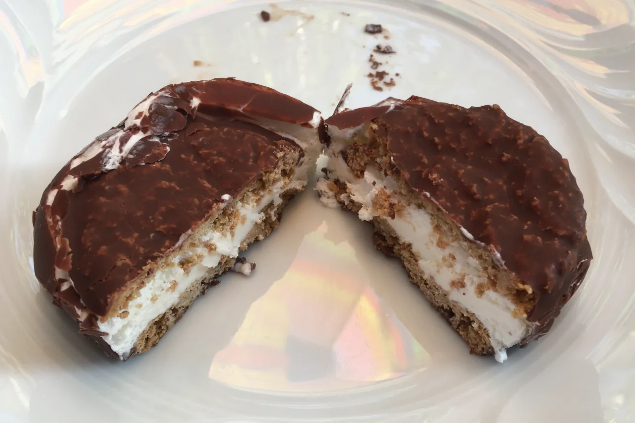 A halved vanilla ice cream sandwich shows chocolate coating, white ice cream, and oatmeal-cookie layers.