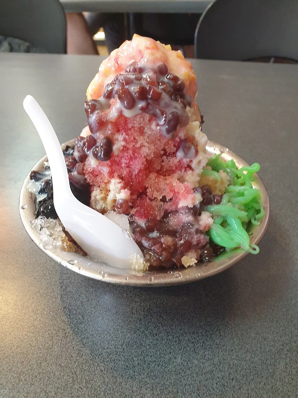 A serving of ice kacang topped with red beans, syrup, and green jelly.