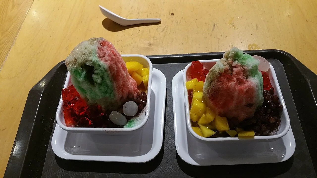 Two bowls of ice kacang with shaved ice, syrup, and colorful toppings on a tray.