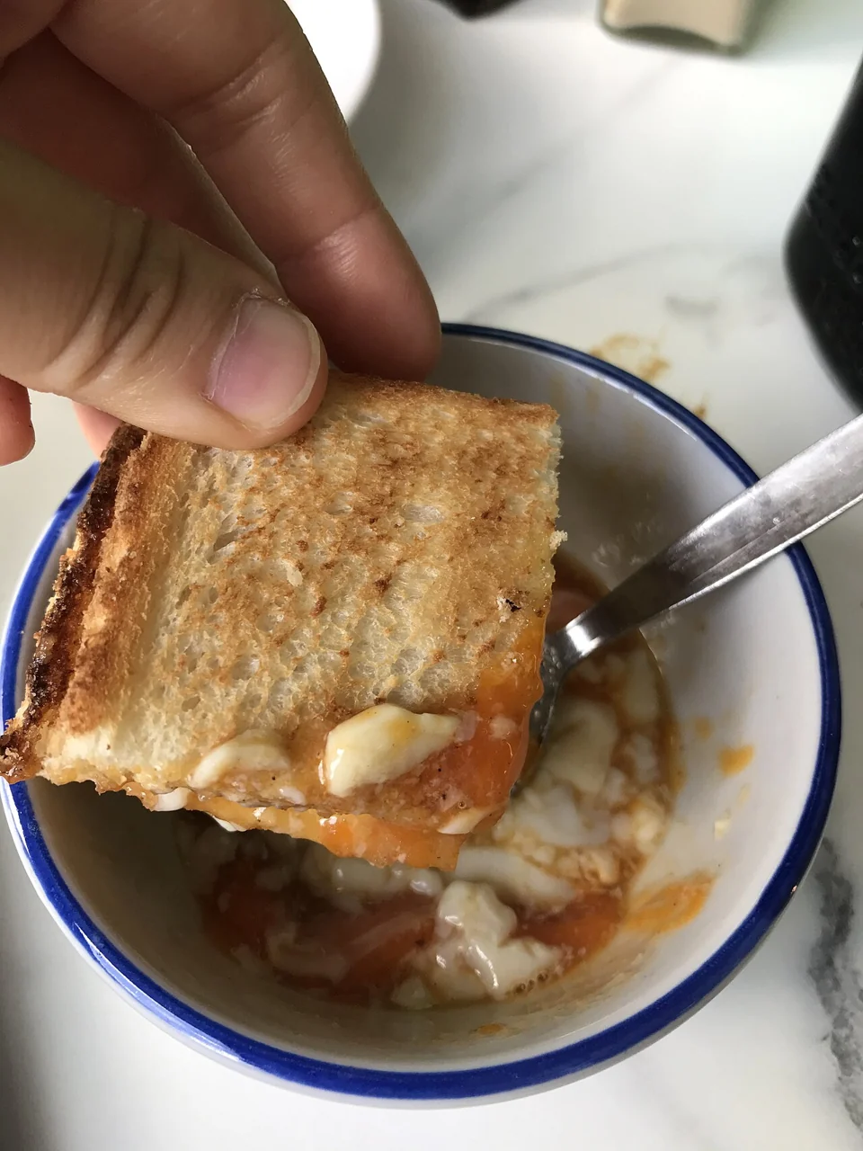 A hand dips a square piece of golden toast into a small bowl of soft-boiled egg.