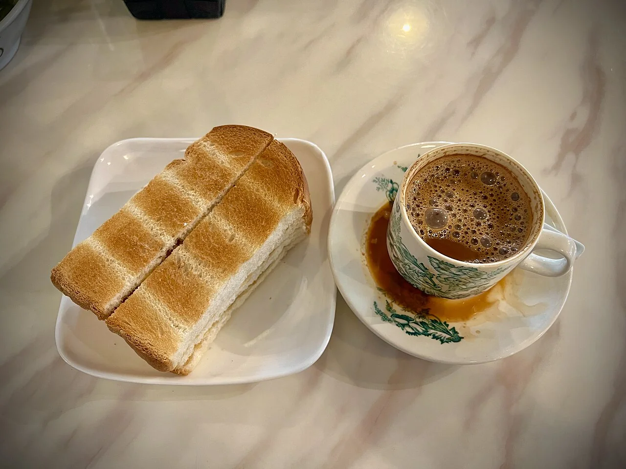 A cup of coffee and kaya toast on a marble table at Yinzo Kopi in Ipoh, Malaysia.