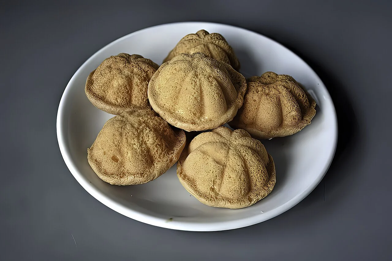 A plate of golden-brown kuih bahulu, small sponge cakes, on a dark surface.