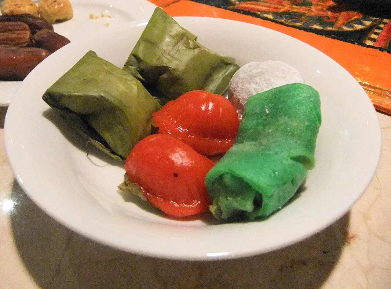 A white plate holds a green rolled kueh dadar among other small sweets.