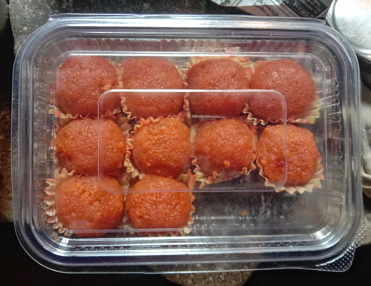 Orange laddus in paper cups fill a clear plastic tray.