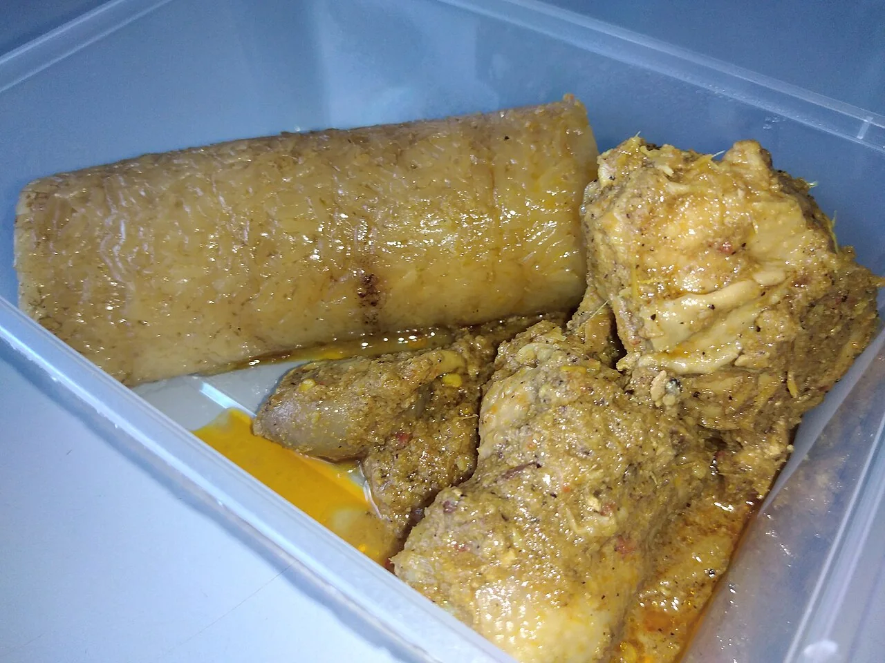 A container with a piece of lemang and chicken rendang.