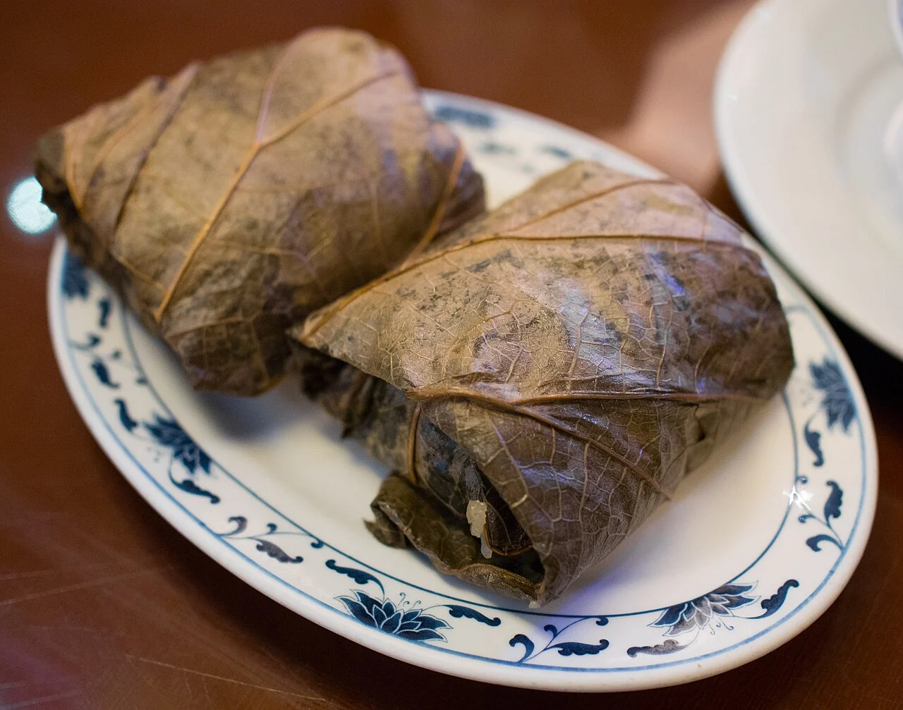 Two parcels wrapped in large dried leaves sit on a blue-and-white plate.