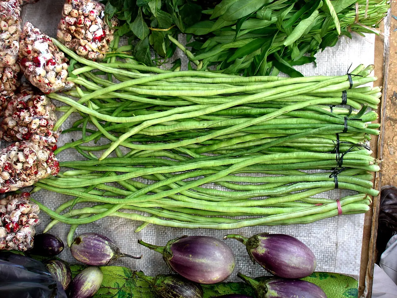 Bundles of fresh green yard-long beans displayed at a market stall.