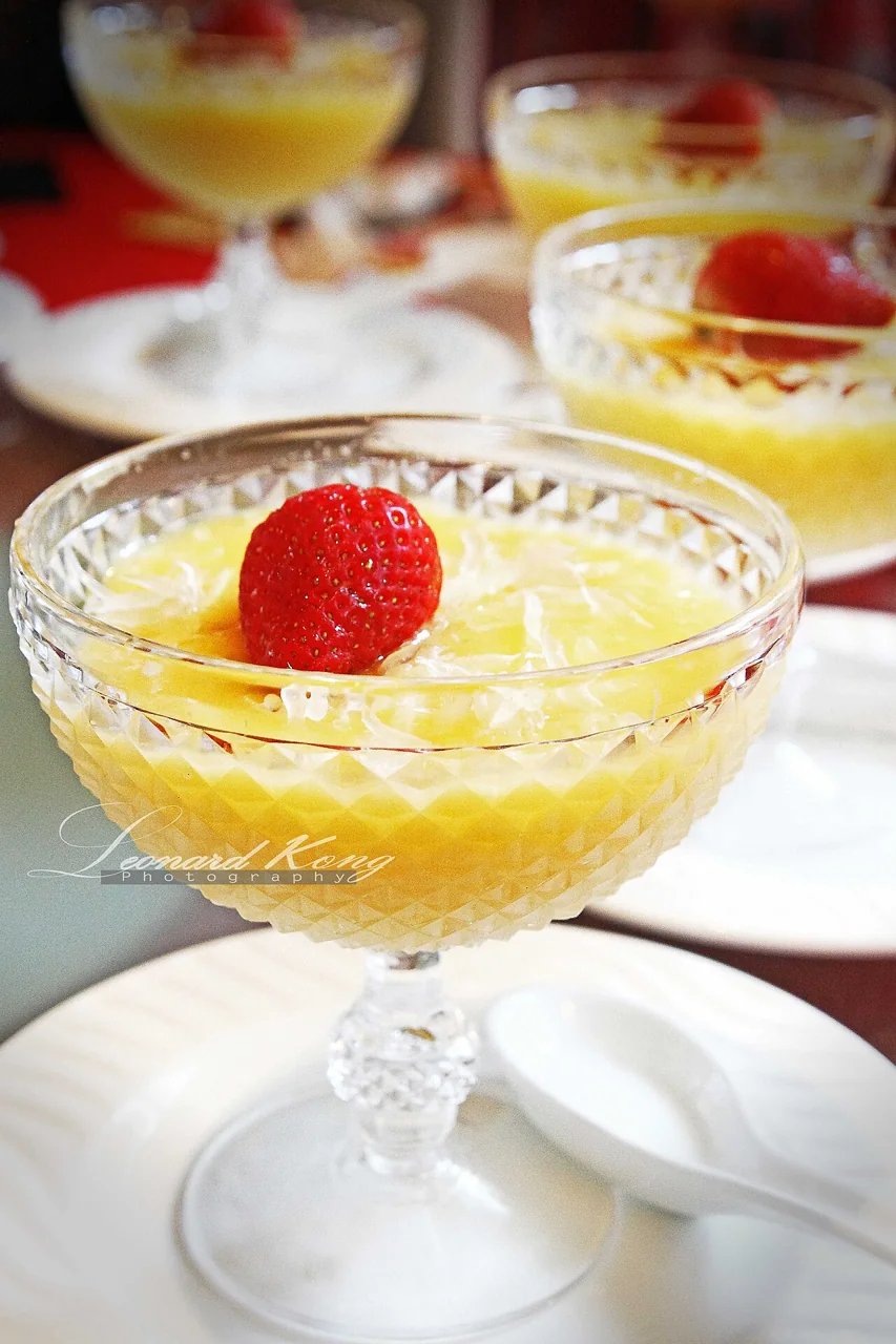 Mango pudding topped with a strawberry served in a clear glass dish.