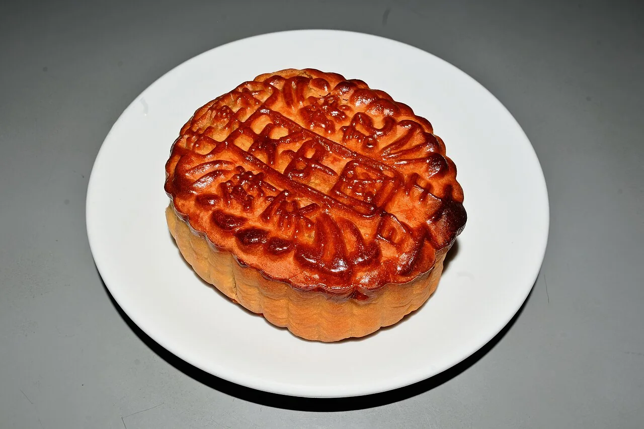 A single golden-brown mooncake with a patterned crust on a white plate.