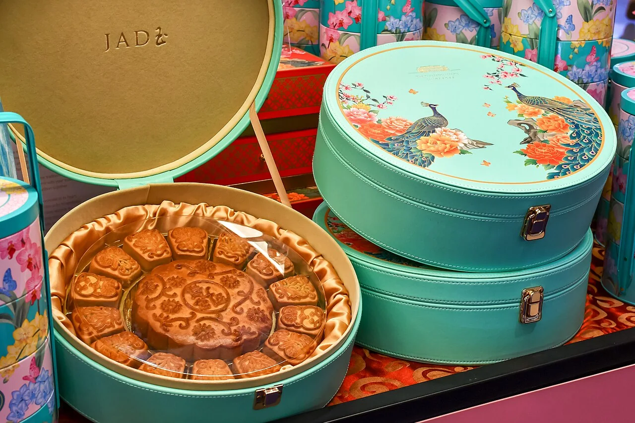 Mooncakes arranged in a round gift box with a peacock-decorated tin beside it.