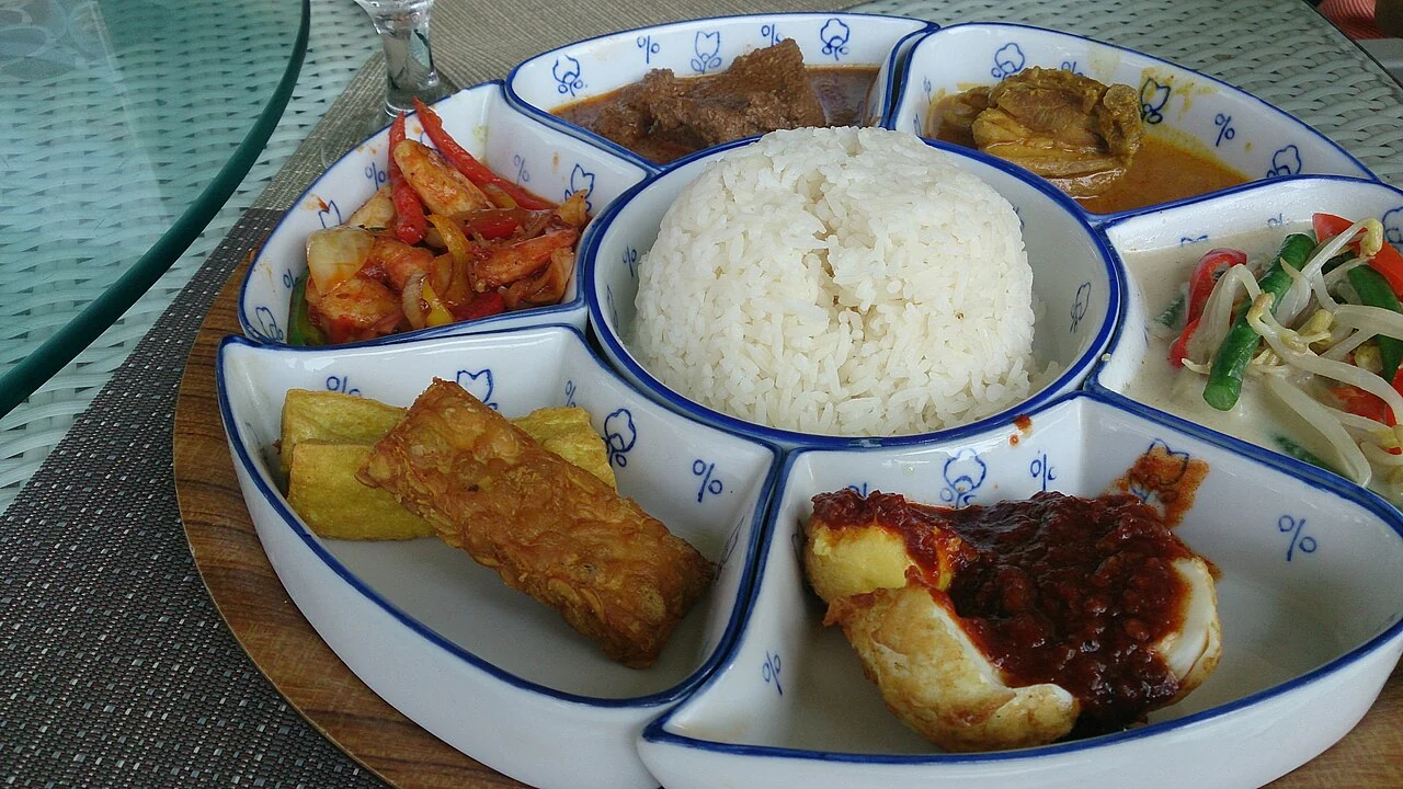 A bowl of white rice sits in the middle of a round tray, surrounded by little dishes of different colours.