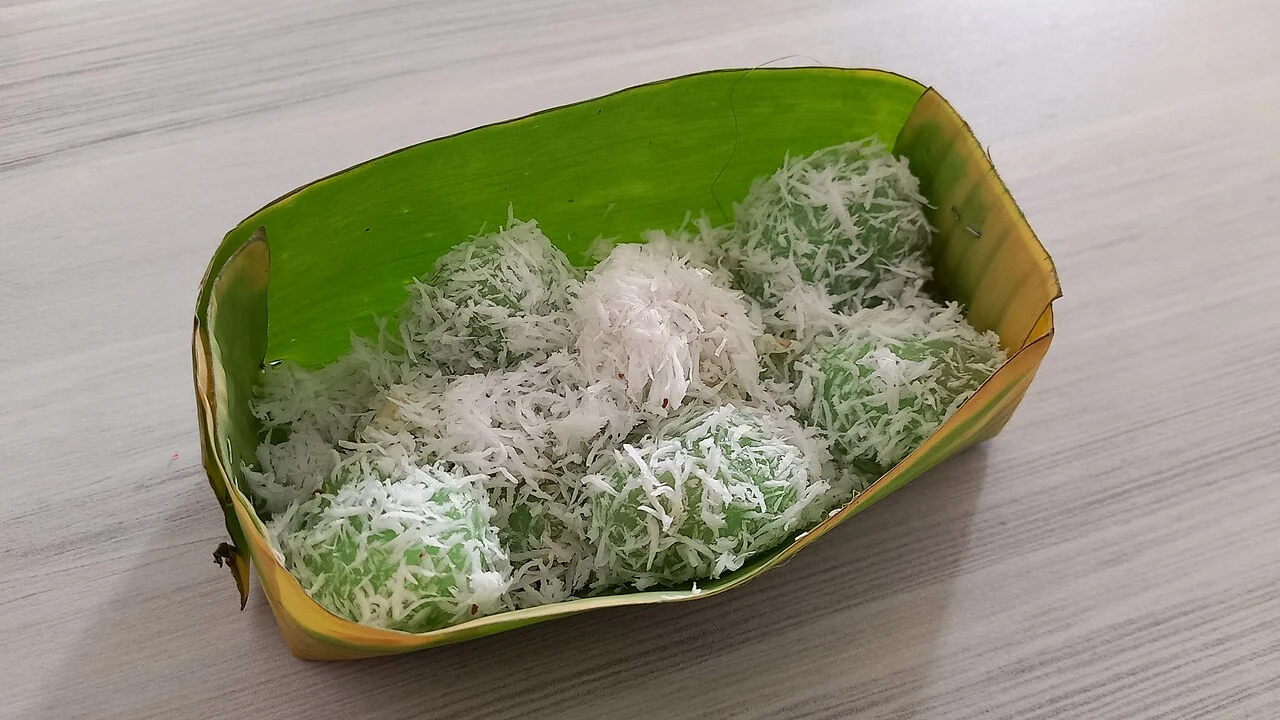 Several green sticky rice balls rolled in white grated coconut sit together inside a folded green banana leaf.