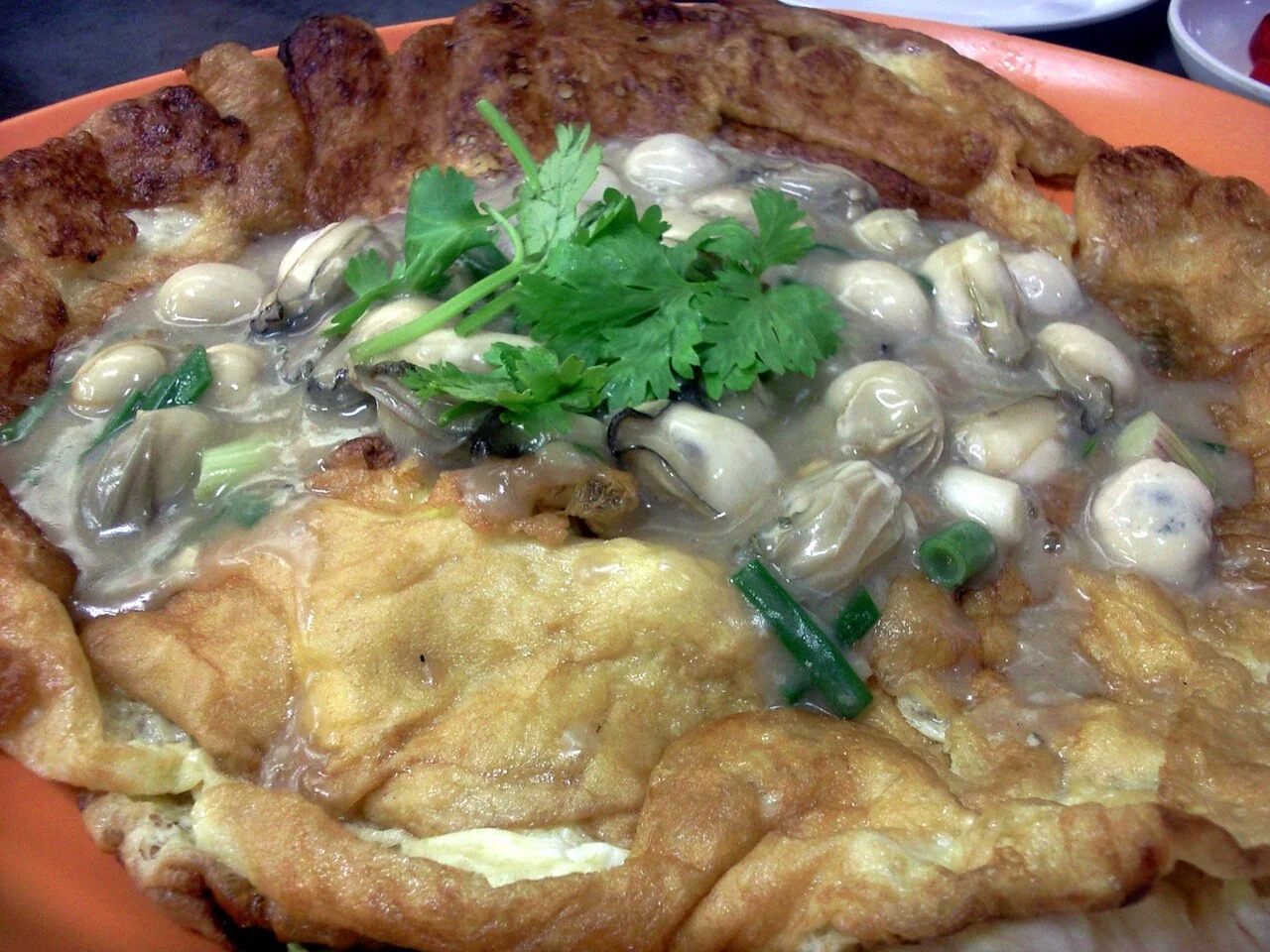 A golden omelette topped with small oysters, green onions and fresh coriander leaves.