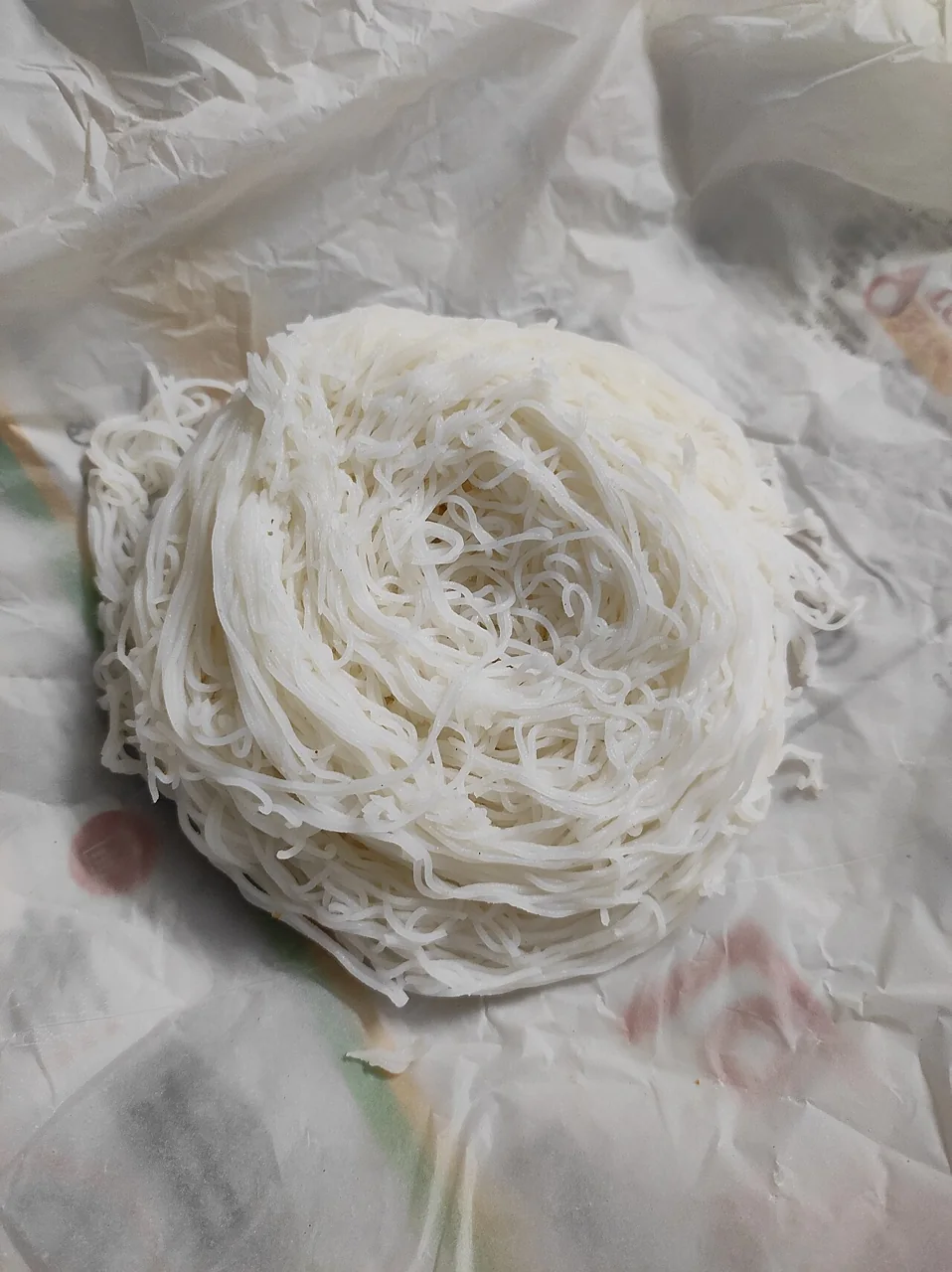 A round mound of white steamed string hoppers on paper.