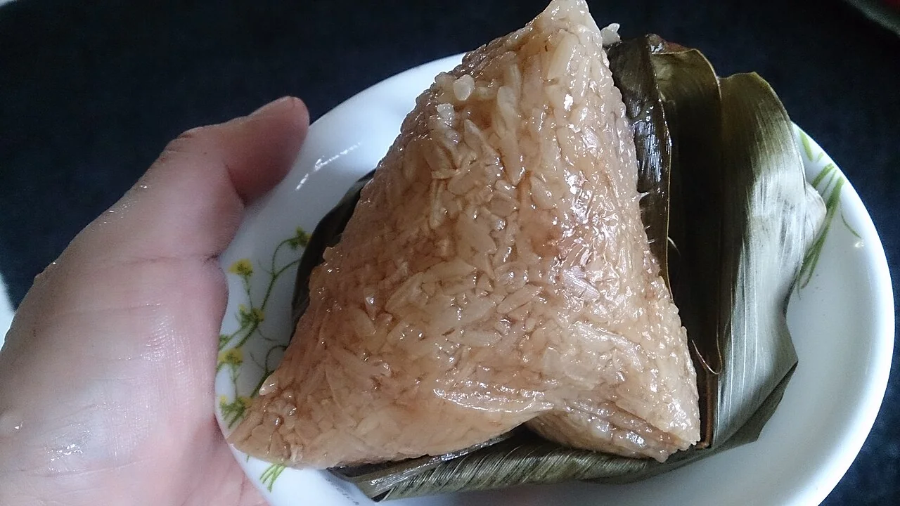 A hand holds a plate with an unwrapped triangular rice dumpling.