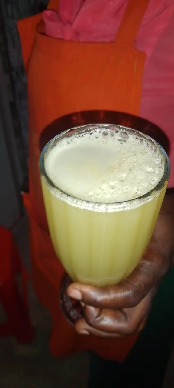 A hand holds a glass of frothy pale sugarcane juice.