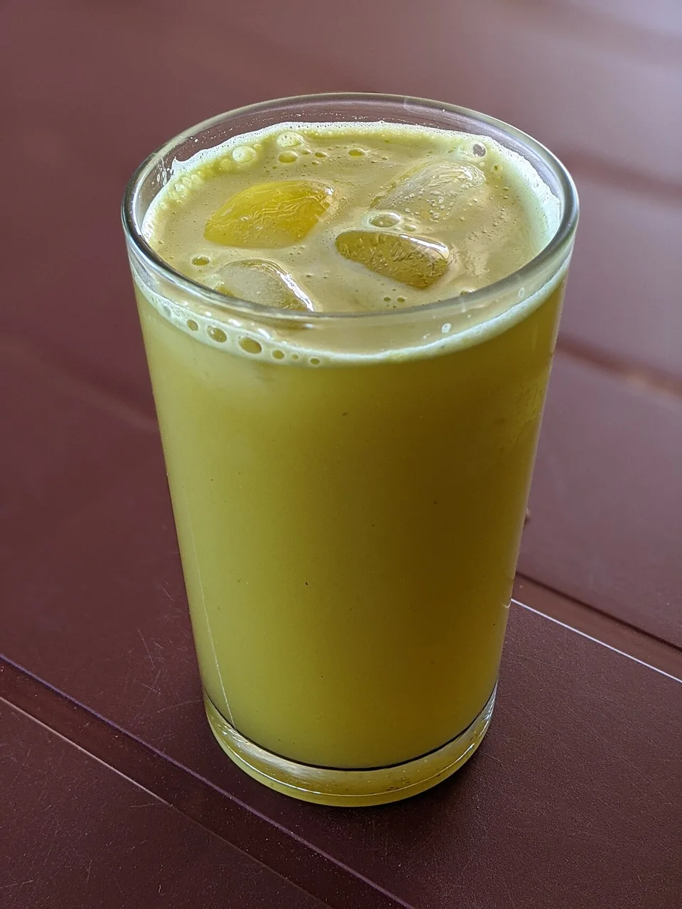 A tall glass of iced sugarcane juice sits on a reddish table.