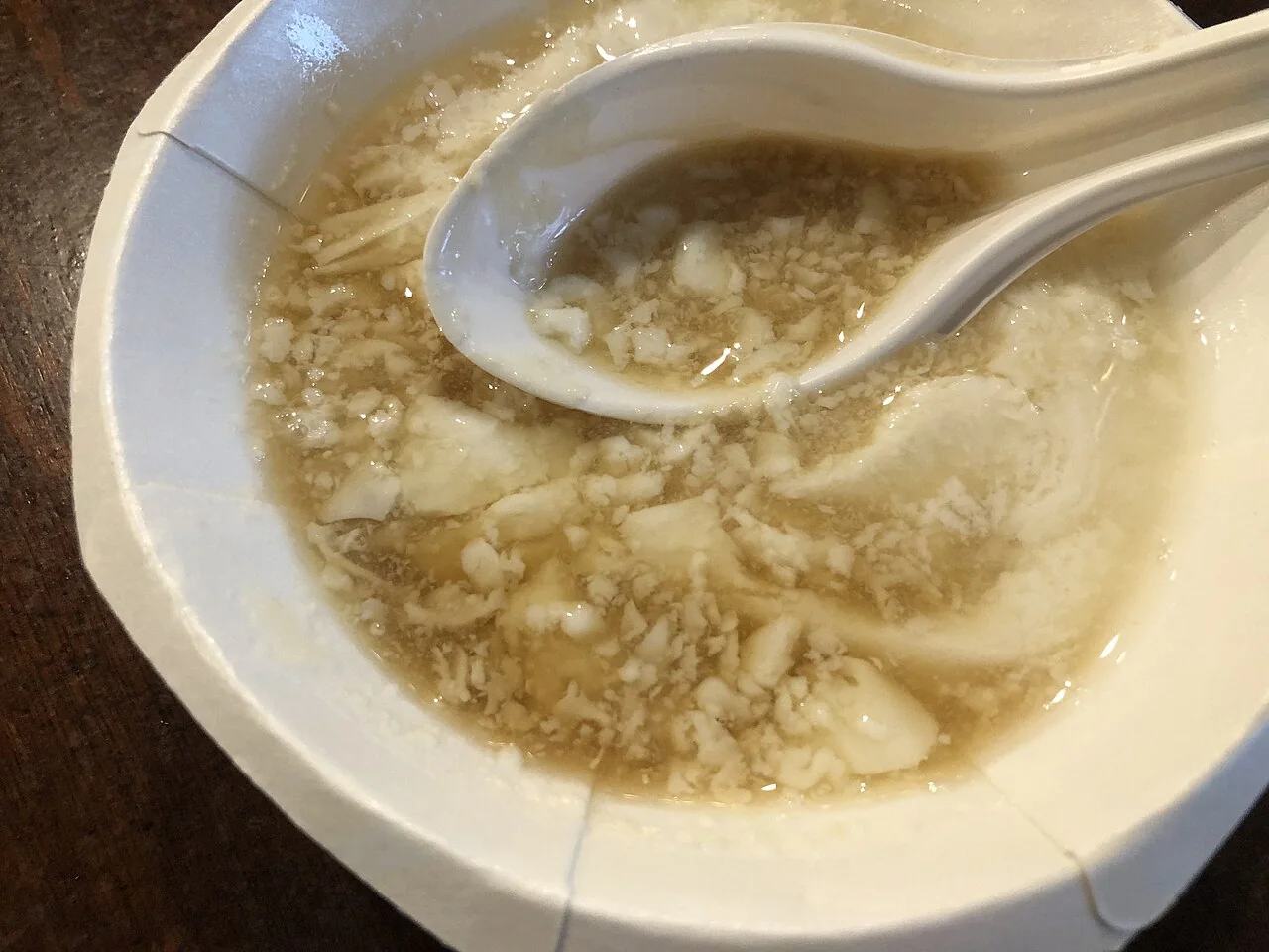 A white bowl holds soft tofu pudding in syrup with a spoon.