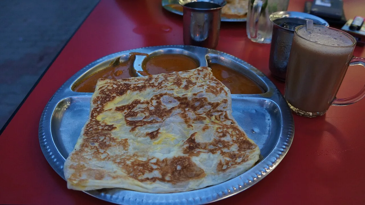 A glass of teh tarik next to a plate of roti telur.