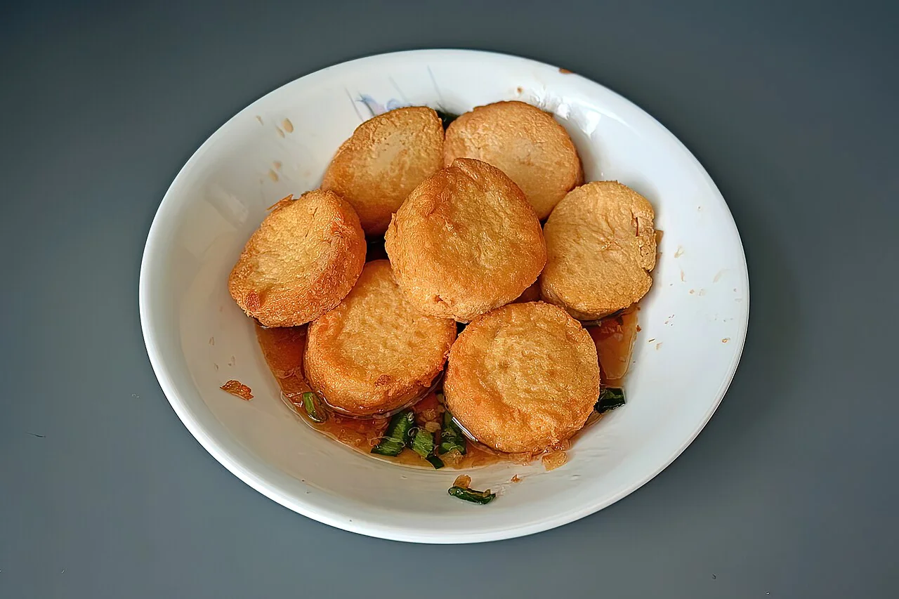 Fried egg tofu slices sit in a white bowl with sauce and scallions.