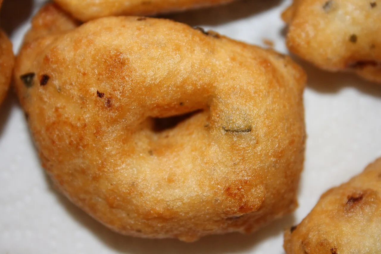 A close-up shows a golden fried vadai with a hole in the centre and small dark speckles.